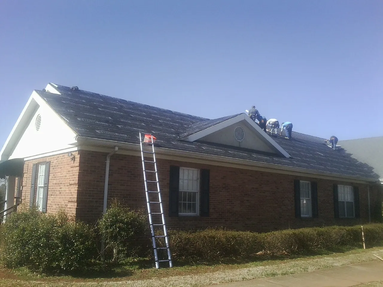 Crew tearing shingles off a brick ranch roof with a ladder set — Emergency Roof Repair work by our crew in Fingal