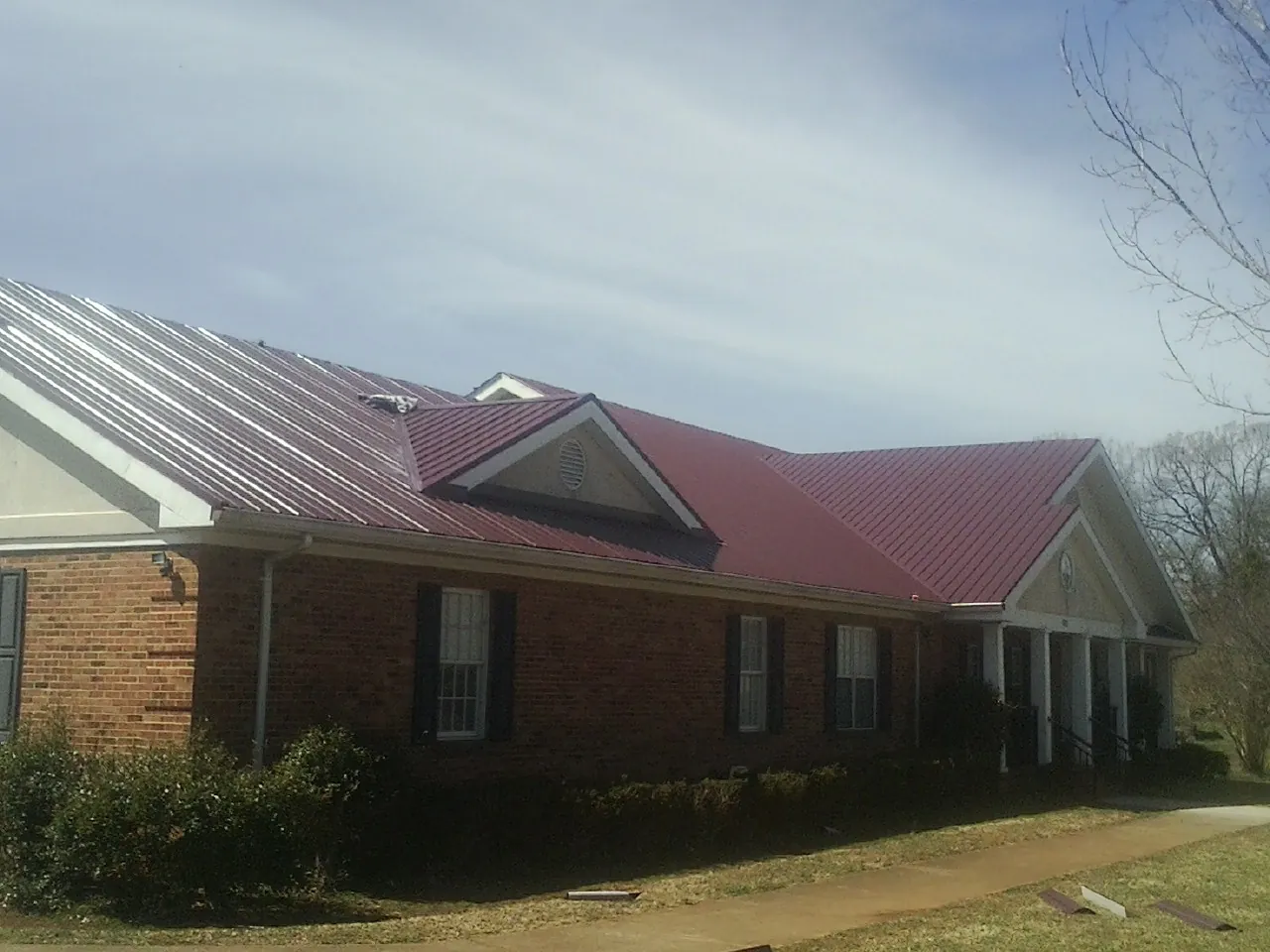 Red metal roof with gabled entries on a long brick building, from a Hail Damage Roof Repair job in Fingal