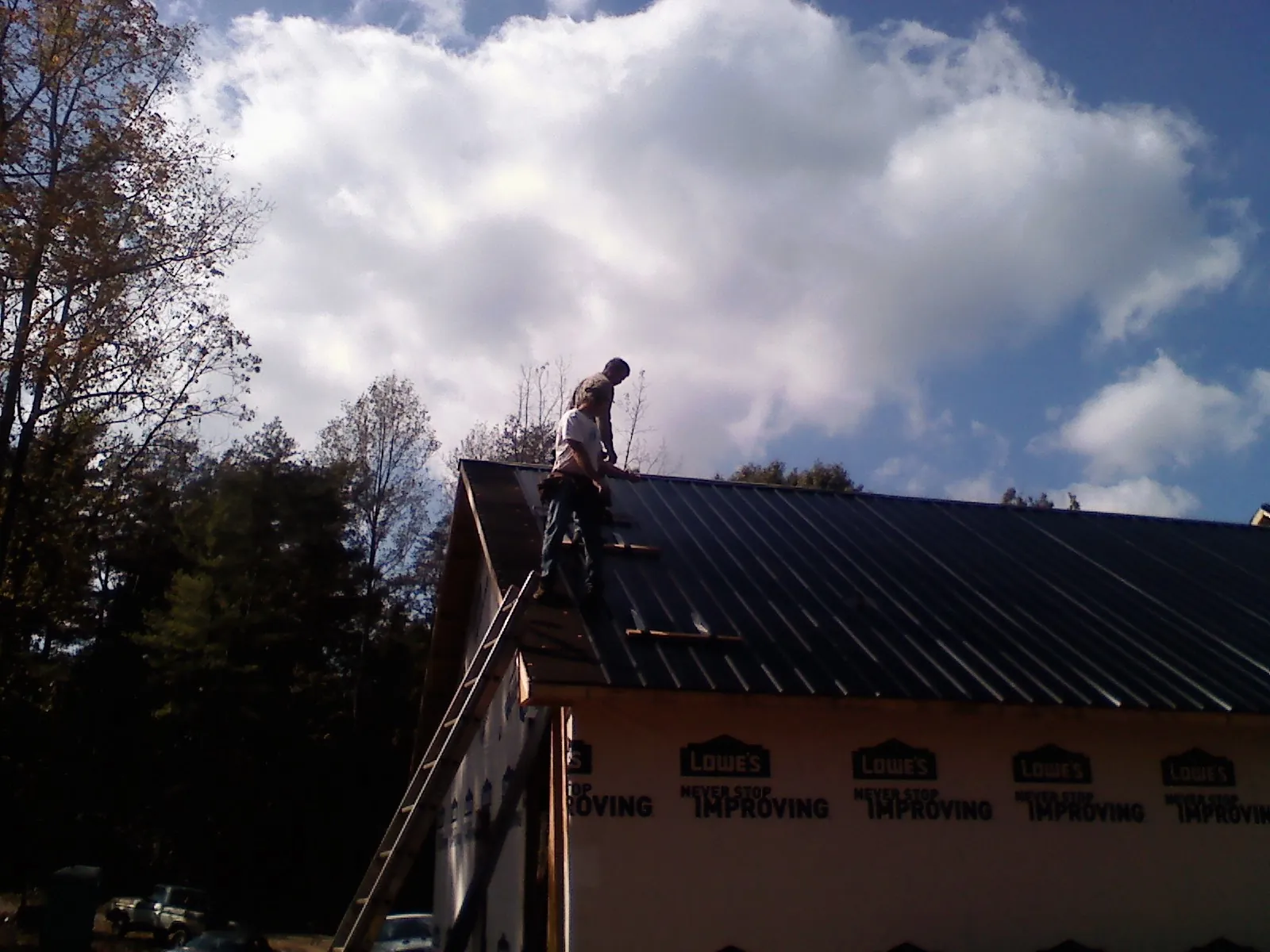 Roofer fastening dark metal panels high against a cloudy sky, from a Roof Inspection job in Fingal