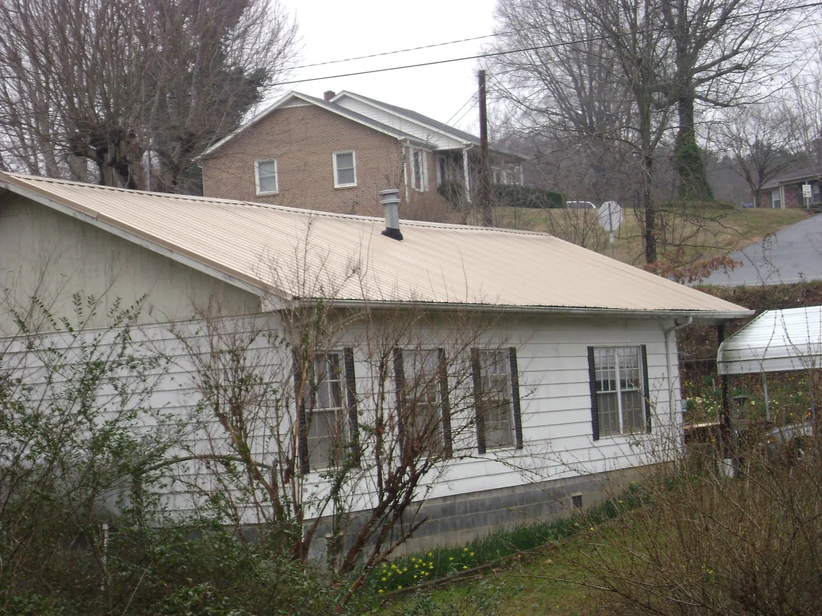 Tan metal roof on a white sided house set into a hillside — Commercial Roofing by Roofing Brothers in Fingal